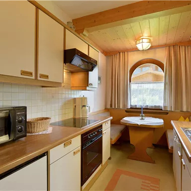 A bright kitchen with wooden shelves, a round table, and a large window. The amenities include a stove, a refrigerator, and a microwave.