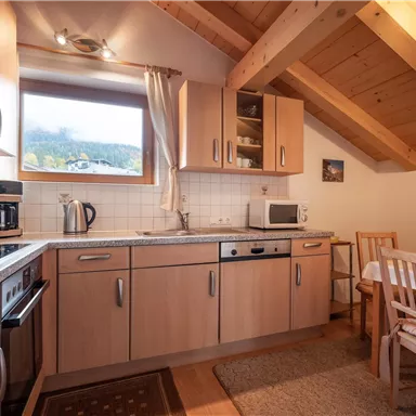 A cozy kitchen with wooden cabinets and modern appliances. A dining table with chairs is located in the corner and offers a view of the landscape through the window.