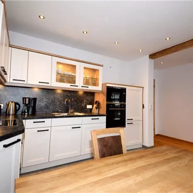 Eine moderne Küche mit weißen Schränken und einer dunklen Arbeitsplatte. Der Essbereich ist mit einem Holztisch und mehreren Stühlen ausgestattet.