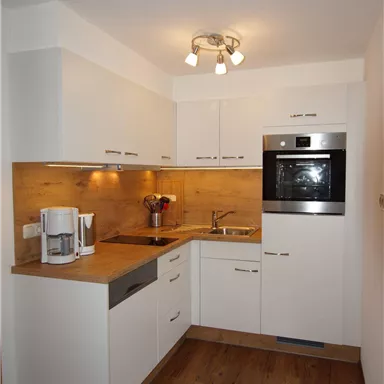 Eine moderne Küche mit weißen Schränken und einer Holzarbeitsfläche. Sie ist mit einem Backofen und einer Kaffeemaschine ausgestattet.