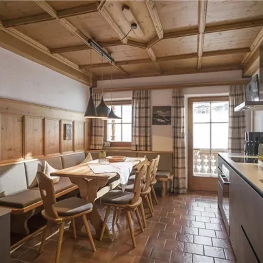 Eine gemütliche Küche mit Holzmöbeln und einem großen Esstisch. Große Fenster sorgen für viel Tageslicht und eine einladende Atmosphäre.