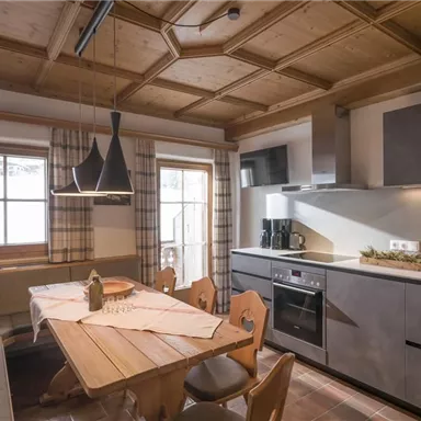 Eine moderne Küche mit Holzdetails und einem großen Tisch. Helle Fenster sorgen für ein einladendes Ambiente.