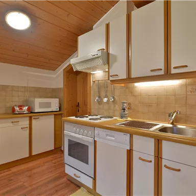 Eine moderne Küche mit Holzverkleidung und hellen Schränken. Sie ist ausgestattet mit einem Herd, einer Spüle und modernen Geräten.