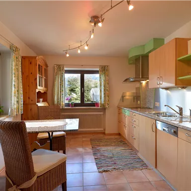 A modern kitchen with wooden and green accents. There is a table with chairs and plenty of natural light from the window.