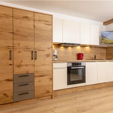 Eine moderne Küche mit Holzschränken und weißen Fronten. Sie ist gut ausgestattet mit einem Herd, einem Kühlschrank und einem Fernseher.