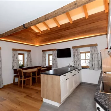 Eine moderne Küche mit Holzregalen und großen Fenstern. Der Raum ist hell und einladend, mit einem Esstisch und komfortablem Ambiente.