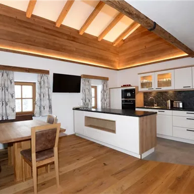 Eine moderne Küche mit Holzverkleidung und einem gemütlichen Essbereich. Helle Farben und große Fenster sorgen für eine einladende Atmosphäre.