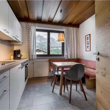 A cozy kitchen with modern furniture and a large window. The view shows impressive mountains in the background.