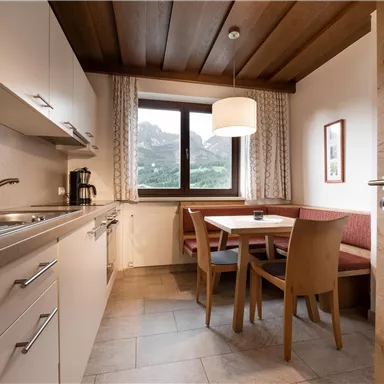 A modern kitchen with a dining area and a window that offers a view of the mountains. The furnishings are simple and functional.