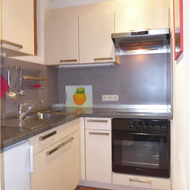 A modern kitchen with bright cabinets and a stove. A colorful picture of an orange hangs on the wall.