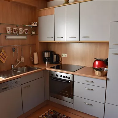 A modern kitchen with wooden furniture and white cabinets. It is well-equipped with a stove, a sink, and various kitchen appliances.