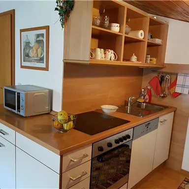 A modern kitchen with wooden shelves and a countertop. On the table, there is a fruit bowl and a microwave.