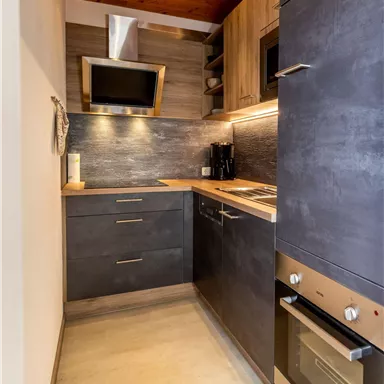 A modern kitchen with a wooden ceiling and elegant, dark cabinets. The amenities include a stove, a refrigerator, and a microwave.