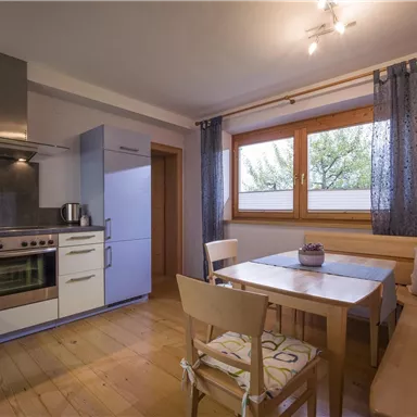 A modern kitchen with wooden flooring and light walls. Next to it, a dining area with a table and chairs.