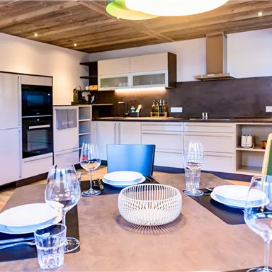 A modern kitchen with elegant furniture and high-quality appliances. The dining table is beautifully set and invites you to eat.