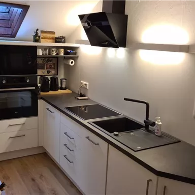 A modern kitchen with white cabinets and black countertops. It is well-lit and features a sink as well as cooking appliances.