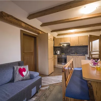 Ein gemütliches Wohnzimmer mit einer hellen Küche und Holzdetails. Ein Essbereich mit einem Holzstich und einer grauen Couch lädt zum Verweilen ein.