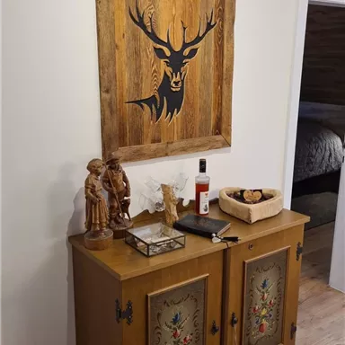 A rustic wooden table with ornate decorations stands against a wall. Above the table hangs a large painting of a deer.