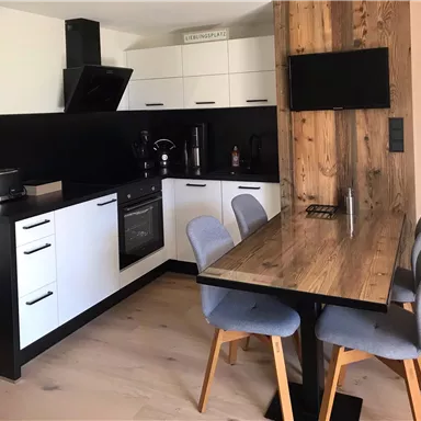 A modern kitchen with white and black furniture. The dining area has a wooden table and upholstered chairs.