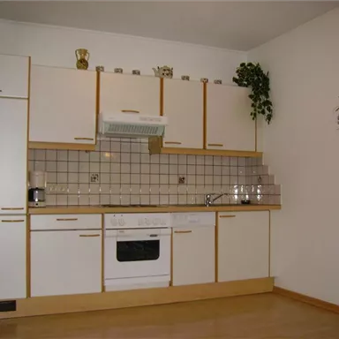 Eine moderne Küche mit weißen Schränken und einem gefliesten Spritzschutz. Auf der Arbeitsfläche stehen einige Küchenutensilien, und der Boden ist aus Holz.