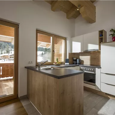 Eine moderne Küche mit Holzdetails und großen Fenstern, die einen Blick auf die winterliche Landschaft bieten. Der Raum ist hell und freundlich gestaltet.