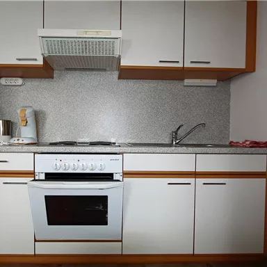 Eine moderne Küche mit weißen Schränken und einer grauen Arbeitsplatte. Der Herd ist unter einem Dunstabzug und es gibt eine Spüle neben dem Herd.