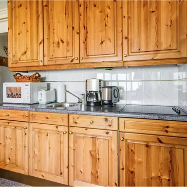 A cozy kitchen with wooden cabinets and modern amenities. In the background, a kettle and a coffee machine are visible.