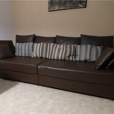 Ein bequemer, brauner Sofa mit gestreiften und einfarbigen Kissen. Der Hintergrund ist in neutralen Farben gehalten.