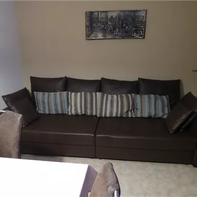 Ein modernes Wohnzimmer mit einem stilvollen braunen Sofa und dekorativen Kissen. Im Hintergrund sind helle Wände und ein Bild zu sehen.