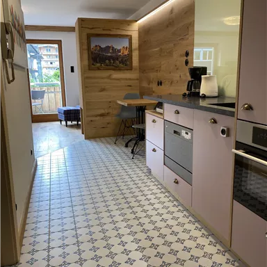 A modern kitchen with light furniture and a beautiful tiled floor. There is a high-quality wood element on the wall.