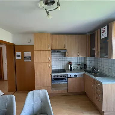 Eine moderne Küche mit Holzschränken und einem Herd. Am Fenster steht eine Kaffeemaschine und die Wände sind hell gefliest.