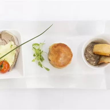 Ein elegantes Gericht mit zartem Fleisch, cremigem Kartoffelbrei und einer kleinen Pastete. Dazu garnieren frische Kräuter und eine Kirschtomate.