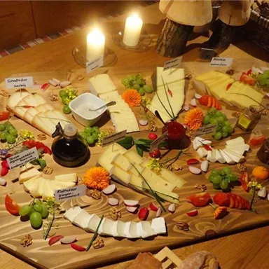 Ein reichhaltiges Käsebuffet mit verschiedenen Käsesorten, Trauben und frischem Gemüse. Die Präsentation ist ansprechend auf einem großen Holzbrett arrangiert.