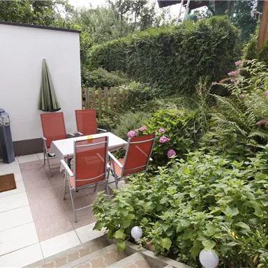 An inviting garden area with a table and chairs. Surrounded by lush greenery and colorful flowers, it creates a relaxed atmosphere.