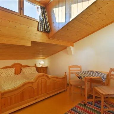 A cozy wooden room with two beds and a small table. The walls are made of wood, and the room has natural light sources.