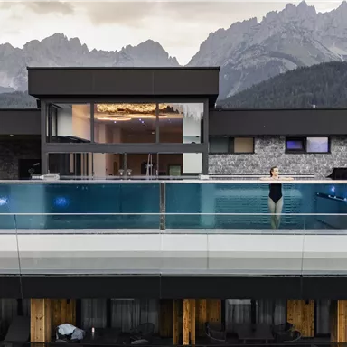 Ein modernes Hotel mit einem Infinity-Pool und einer atemberaubenden Berglandschaft im Hintergrund. Die Architektur ist zeitgemäß und elegant.