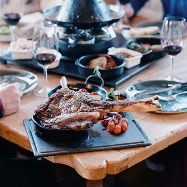 Ein reichhaltiges Abendessen mit Fleisch, Gemüse und mehreren Beilagen auf einem Tisch. Rotwein und Glaswaren ergänzen die festliche Atmosphäre.