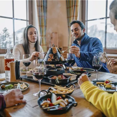 Ein gemütliches Essen in einer Berghütte mit Freunden. Auf dem Tisch stehen verschiedene Köstlichkeiten und Weingläser.