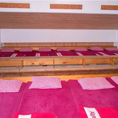 A sleeping area with red mattresses and checked pillows. The walls are simple and the atmosphere is cozy.
