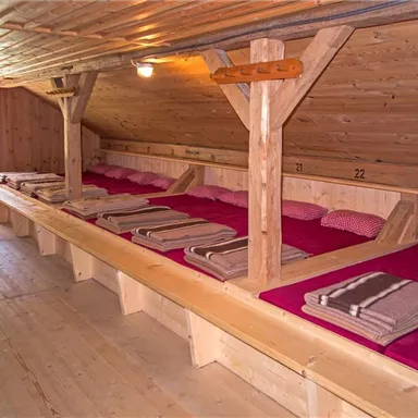 A cozy sleeping room with several wooden beds. The beds are equipped with red pillows and blankets.