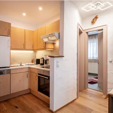 A modern kitchen with wooden cabinets and appliances. The room is bright and welcoming with access to another room.
