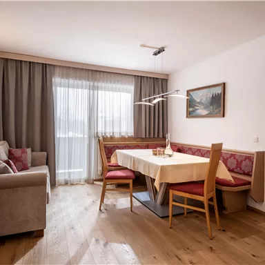 A cozy living area with a dining table and red chairs. Large windows let in a lot of light and create an inviting atmosphere.