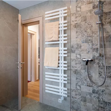 A modern bathroom with a shower and a towel holder. The walls are clad with decorative tiles.