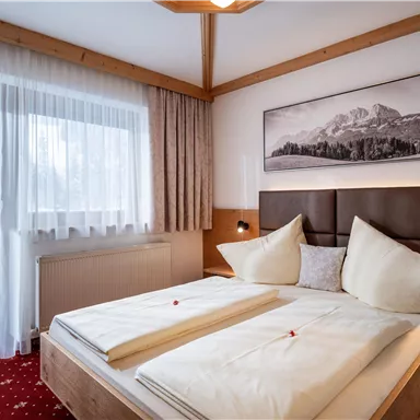 A cozy bedroom with a double bed and wooden details. The large window lets in plenty of light and offers a view of the mountains.