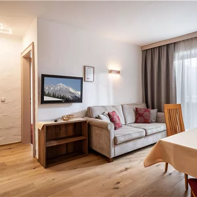 A modern living room with a cozy sofa and a wooden table. Large windows let in plenty of daylight.