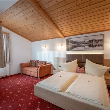 Ein gemütliches Hotelzimmer mit Holzdecke und roten Teppich. Das Zimmer verfügt über ein Doppelbett, eine Sitzecke und ein Bild an der Wand.