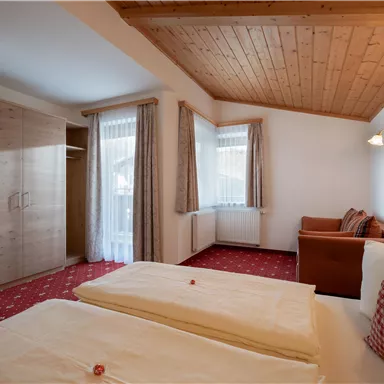 Ein gemütliches Schlafzimmer mit zwei Betten und einem Kleiderschrank. Das Zimmer hat große Fenster und einen hellen Holzdecken.