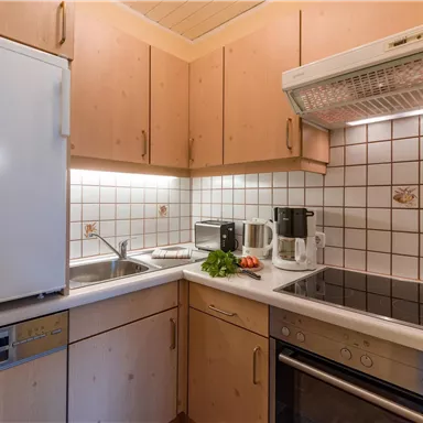 Eine moderne Küche mit Holzschränken und weißen Kacheln. Sie ist mit einem Kühlschrank, Herd und Küchenutensilien ausgestattet.