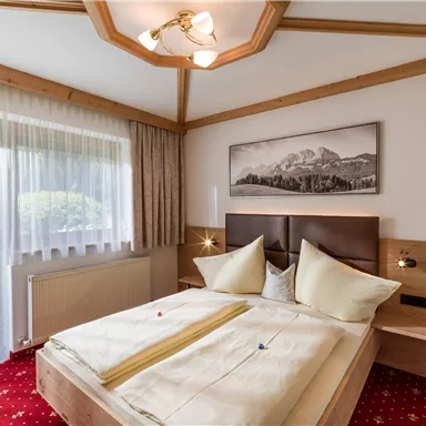 Ein gemütliches Schlafzimmer mit einem Doppelbett und modernen Möbeln. Große Fenster lassen viel Tageslicht herein und bieten einen Blick nach draußen.