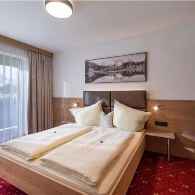 Ein modernes Schlafzimmer mit zwei Betten und eleganter Holzverkleidung. Das Zimmer ist hell und freundlich, mit einem großen Fenster und einem dekorativen Bild an der Wand.